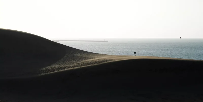 一位旅行者在沙漠上看著海景
